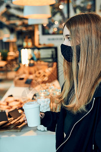柜台买喝妇女拿着咖啡杯站在店排队等待命令戴面罩以避免感染和防止疾病在出现冠状毒时传播的人在咖啡店里站成排队等待秩序佩戴面罩以防止图片