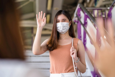 身戴外科面具的亚洲年轻女乘客在Covid19疫情爆发社会动荡与新常态概念等大城市旅行时用手挥向地铁列车朋友打招呼图片