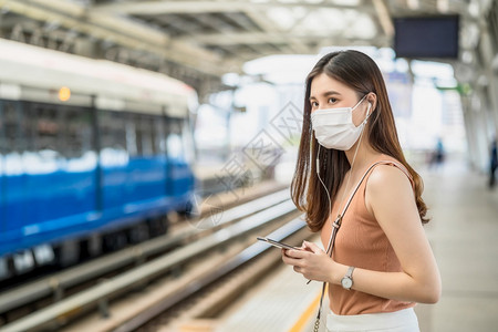电话游客新冠在Covid19爆发感染和大流行病概念的都市旅行时身戴外科面具并通过地铁火车智能手机监听音乐的亚洲女青年乘客在Cov图片