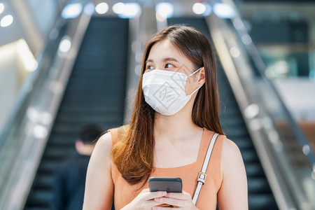 韩国人年轻的脸亚洲女乘客在Covid19疫情爆发的大城市旅行时身戴外科面具用智能手机在扶梯前使用智能移动电话行走之间通过地铁交接图片