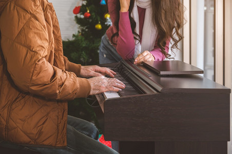 盛大两人在客厅享受愉快的时光与钢琴男一起弹为妇女唱歌在家里庆祝冬季节日她们在家一起庆祝冬季节日窗户女士图片