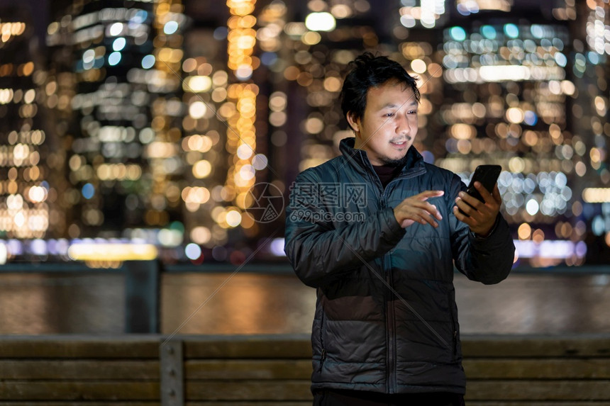 想象消息传递身穿大衣西装的亚洲男子使用智能手机与微笑动作在东河美国市区附近纽约城风景模糊的照片上拍下笑容事业无处不在的概念专业图片