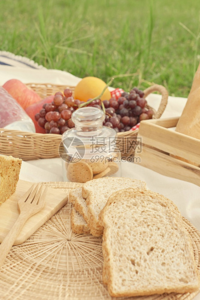 爱白布上野餐包括一篮子水瓶苹果橙子和葡萄面包一罐饼干和面包片等这是野餐概念乐趣农村图片