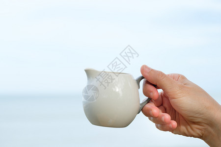 陶瓷制品优点手握在海和天空背景上带着和平喜悦的概念用手举着陶瓷杯咖啡放松图片