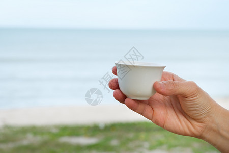 手握在海和天空背景上带着和平喜悦的概念用手举着陶瓷杯咖啡成人肖像假期图片