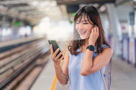 亚洲妇女通过智能移动电话和在铁路站平台生物测量核查和人工智能概念监听音乐利用面部识别和听音乐的亚裔妇女使用智能手机进行面部识别生图片