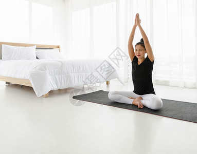 简单的在家做瑜伽冥想锻炼的亚洲妇女坐在轻松椅姿势或Sukhassana穿着黑衬衫和白裤子在色卧室头部举起手顶姿势的苏哈萨娜正念达图片