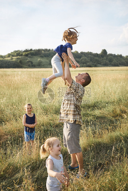 天人们父亲把小女孩扔在空中家庭一起花时间在草地上亲近自然父母和孩子一起玩Candid人游戏真实的时刻情境开支图片