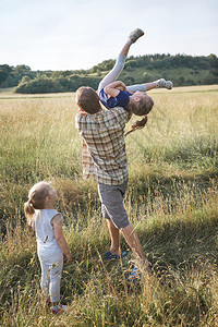 父亲把小女孩扔在空中家庭一起花时间在草地上亲近自然父母和孩子一起玩Candid人游戏真实的时刻情境快乐的棉花糖季节图片