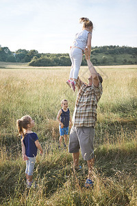父亲把小女孩扔在空中家庭一起花时间在草地上亲近自然父母和孩子一起玩Candid人游戏真实的时刻情境戳闲暇女图片