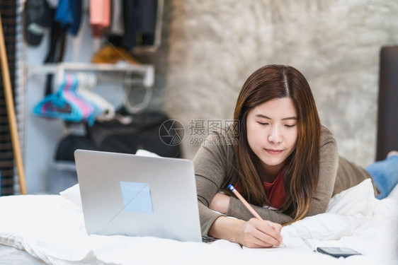 亚洲商业妇女利用技术笔记本电脑和写作在家工卧室自由与企业家创者和企家新创办商和企业主生活方式职业社会距离和责任中从事家庭工作网络图片