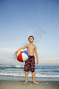 男孩在海滩上拿着沙滩球图片