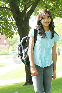 年轻女孩带着背包站在树上 微笑着青少年晴天精力中学学生孩子混血背景图片