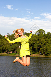 快乐的姑娘跳到河岸上空气幸福成人蓝色自由喜悦运动员假期运动微笑图片