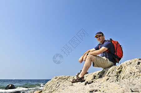 在岩石上坐着的希克人男性活动背包冒险海洋成人远足者娱乐旅行图片