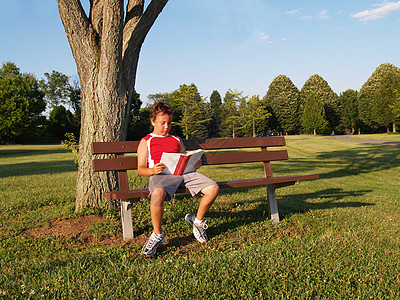 年轻男孩在公园长椅上看书图片