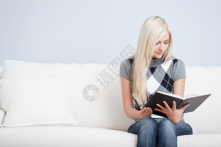 坐在索法阅读书上的年轻妇女长发幸福女士沙发蓝色客厅成人快乐公寓女性图片
