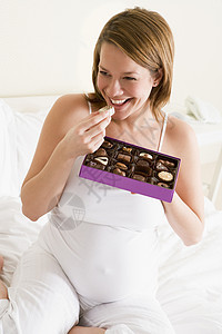 在床上吃巧克力的孕妇笑着在床上新妈妈享受怀孕妈妈母亲卧室糖果家庭孕妇装孕产图片