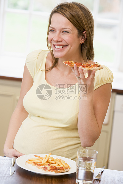 厨房的孕妇吃薯条和比萨面带微笑怀孕孕产披萨享受女性家庭妈妈准妈妈筹码食物图片