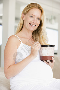 怀着一桶冰淇淋微笑的孕妇妈妈享受准妈妈孕产新妈妈饮食待产家长怀孕孕妇装背景图片