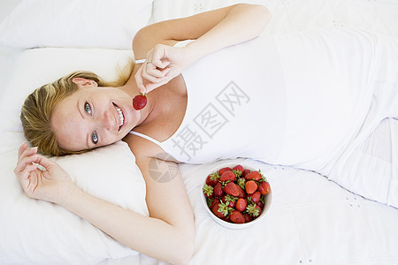 躺在床上的孕妇带着一碗草莓 微笑着水果孕产家庭相机卧室怀孕新妈妈小吃女性待产图片