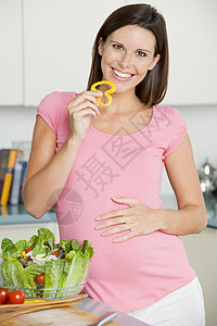 在厨房做沙拉和微笑的孕妇在厨房里准妈妈家长孕产相机女性新妈妈怀孕家庭孕妇装蔬菜图片