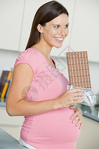 厨房里有大巧克力棒的孕妇笑着在厨房里孕妇装新妈妈巧克力孕产怀孕家庭准妈妈家长享受饮食图片