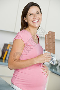 厨房里有大巧克力棒的孕妇笑着在厨房里怀孕孕产饮食家庭小吃准妈妈巧克力妈妈孕妇装女性图片