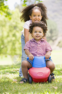姐姐带着车的笑容推着弟弟在玩具上玩耍图片