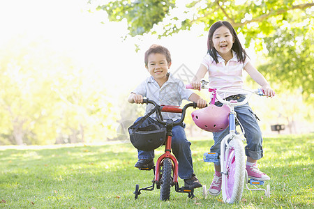 哥哥和姐姐在户外的自行车上微笑着笑男性男生乐趣头盔女性享受女孩公园相机水平图片