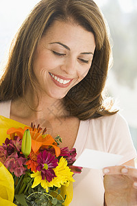 妇女拿着鲜花和看书时微笑图片
