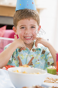 参加派对的年轻男孩坐在餐桌边 笑着食物生日孩子男生孩子们小男孩相机男性桌子微笑图片
