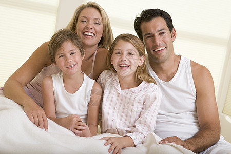 家人在床上微笑地坐在床上孩子父亲四个人亲热家庭生活男性女性孩子们卧室感情图片