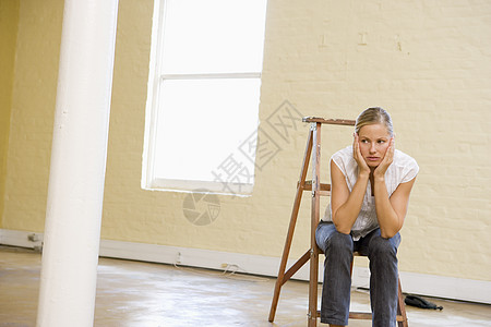 坐在空旷空间的梯子上的妇女看着无聊图片