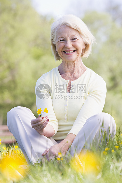 女人坐在户外微笑着笑着 拿着一朵 Buttcup花女性农村采摘场地毛茛女士公园花朵野花退休图片