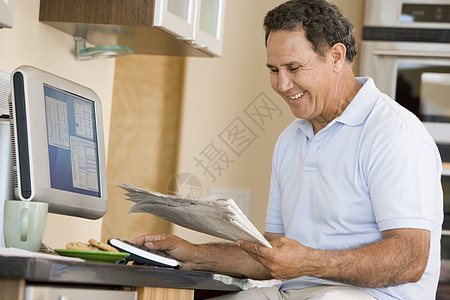 厨房里的男人带着电脑和报纸笑着微笑工作站退休冲浪成人时事互联网阅读技术水平桌子图片