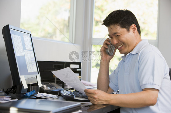 家中办公室有电脑和文件的男子在电话上笑着图片