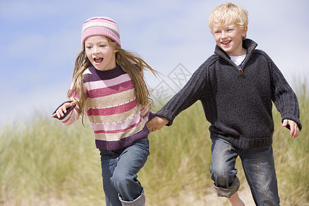 两个小孩在海滩上微笑着手笑着跑的幼童视角衣服女性踪迹低角度孩子季节中年沙丘自由图片