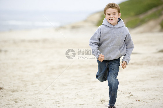 在海滩上微笑的年轻男孩跑步海岸活力海洋相机孩子们小男孩季节衣服男性图片