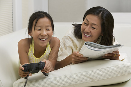 母亲和女儿玩视频游戏和在库奇阅读图片