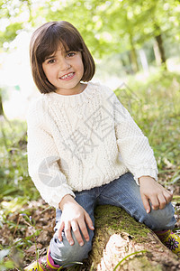 坐在树木上笑着的树林里的年轻女孩微笑林地雨靴女性公园农村森林孩子靴子孩子们图片