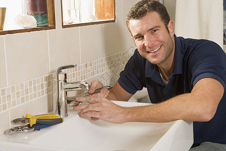 在水槽上工作的木材工人笑着管道洗手盆微笑商业男性生意男人活动长度浴室图片