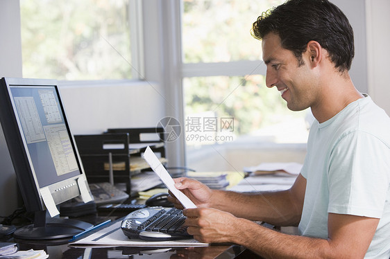 家庭办公室的男职员使用计算机手持文件并微笑图片