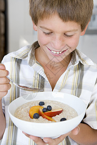 厨房里的小男孩在吃燕麦和水果 笑着的果实孩子们食品健康饮食浆果早餐麦片一个男孩食物饮食儿童图片