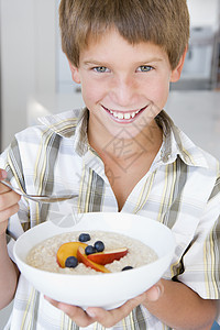 厨房里的小男孩在吃燕麦和水果 笑着的果实食品食物浆果稀饭微笑麦片一个男孩早餐儿童孩子们图片