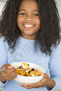 坐在厨房的年轻女孩吃着一碗水果 微笑着饮食食物一个女孩儿童零食沙拉果盘健康饮食孩子们孩子图片