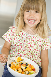 坐在厨房的年轻女孩吃着一碗水果 微笑着沙拉一个女孩果盘食品食物女性饮食零食儿童享受图片