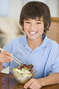 饭厅的年轻男孩在吃中国食物时微笑着笑小男孩食品用具刀具饮食餐具中餐一个男孩外卖儿童图片