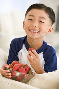 小男孩在客厅吃草莓时微笑着笑头肩享受偏移角食物孩子们食品儿童孩子健康饮食水果图片