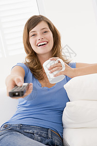 妇女用遥控器和咖啡在客厅里微笑着的咖啡图片